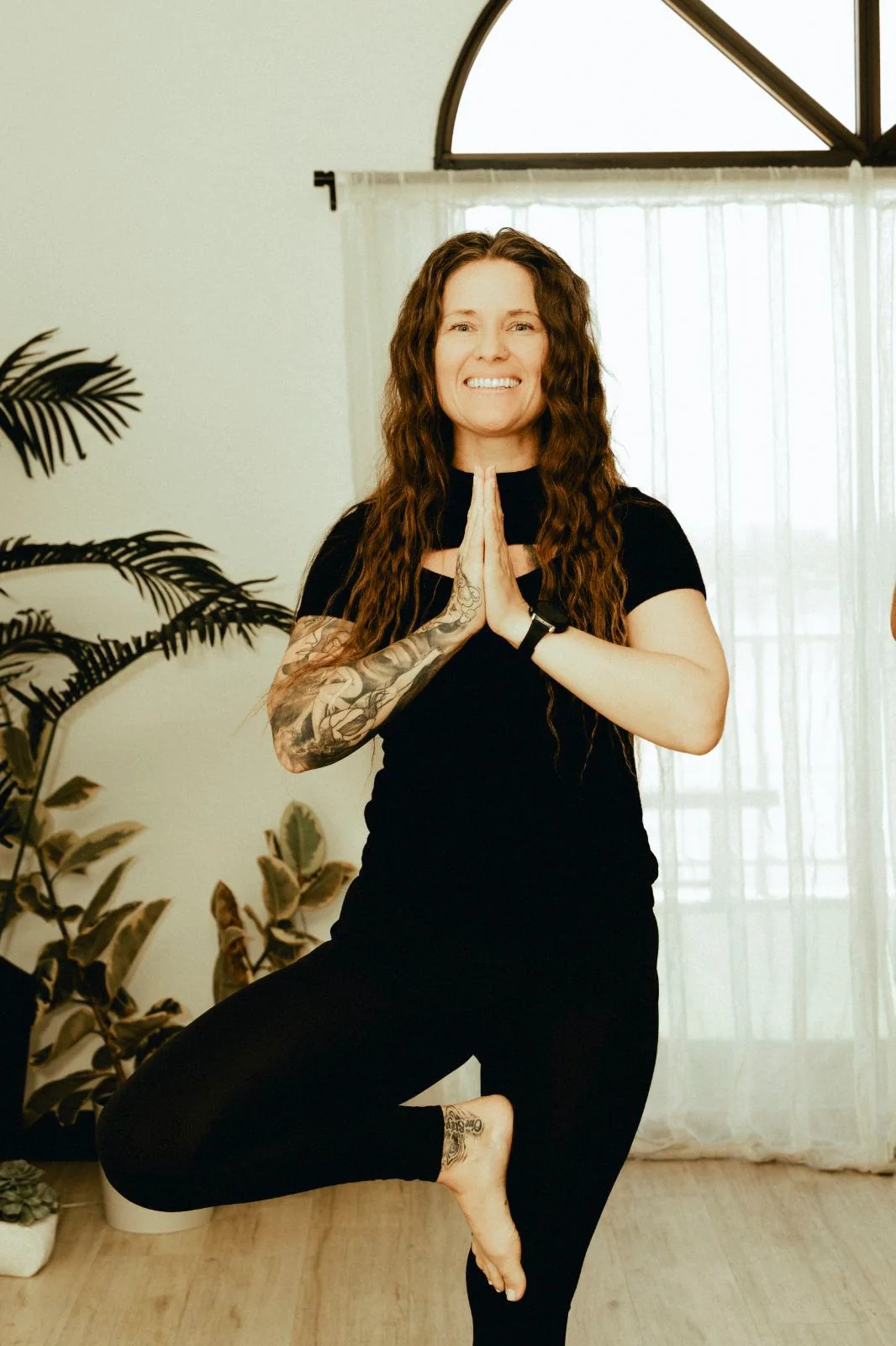 Tiffany Lehman smiling while practicing tree pose in a bright studio